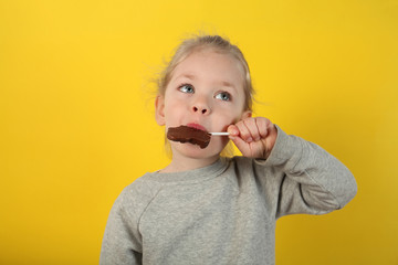 Cute girl child eating sweet chocolate candy on yellow background. Happy childhood.