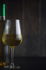 Transparent bottle of white dry wine on the table. White wine glass on a wooden background.