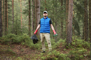Naklejka na ściany i meble Adult man volunteer in red gloves removes plastic trash in forest, caring for environment.