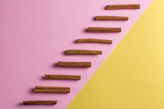 Row Of Cinnamon Sticks From Above On A Bright Yellow And Pink Background. Copy Space