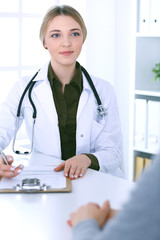 Young woman doctor and patient at medical examination in hospital office. Khaki colored blouse of therapist looks good. Medicine,  healthcare and doctor's appointment concept