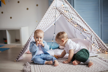 Couple of small infant boys of 1-year old playing alone in wigwam tent with garland at nursery in home interior. © alfa27