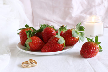 Bright wedding scene, porcelain plate with with fresh strawberries and wedding rings a white background. Feminine styled stock photo.