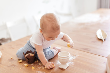 Adorable little helper cooking in kitchen. Cute little toddler crawling on kitchen table, covered...