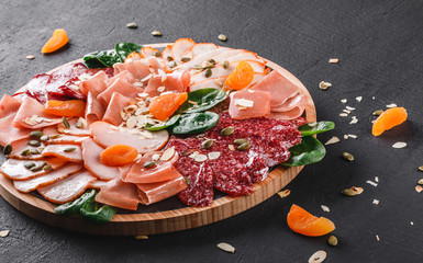 Antipasto platter cold meat, prosciutto, slices ham, beef jerky, salami, meat and nuts on cutting board over black stone background. Meat appetizer, catering food concept
