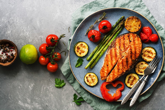 Grilled Salmon With Vegetables Zucchini, Asparagus, Tomato, Sweet Pepper On A Plate, Gray Background. Overhead View