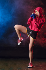Female blonde boxer in pink hoodie prepares to kick at a boxing studio. Woman boxer in motion over...