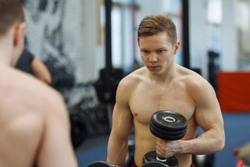 Fototapeta na wymiar Young, athletic guy lifting dumbbells in the gym.