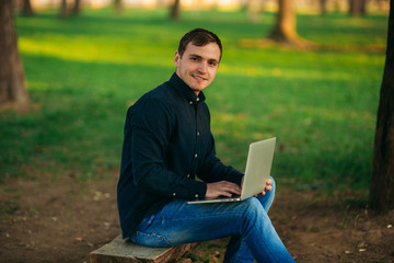 Programmer working in the park on laptop. Man sitting on bench
