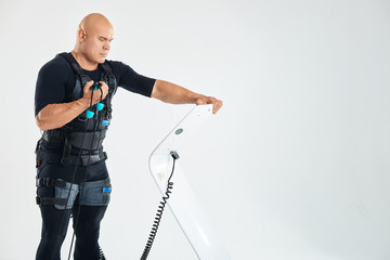 brutal male athlete working out with EMS vest and looking at the screen of the machine. close up photo. copy space. heaalth and body care