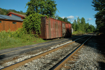 Fototapeta na wymiar Abandoned railway boxcar on siding, rail tracks and trees