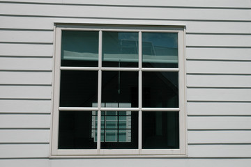 White 9 pane window with reflections in clapboard siding