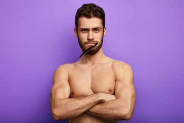 Fototapeta premium brutal serious man with toothbrush in mouth and crossed arms looking at the camera. isolated over blue background