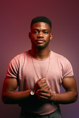 Serious black Afro American man with thoughtful expression looking directly into camera while posing against dark studio wall. Grave sportsman in t-shirt planning day schedule