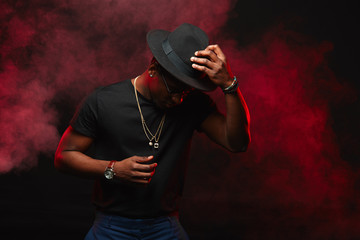 Portrait of handsome young african DJ or jazz musician in creative hat in black t-shirt on dark...
