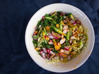 Top view on bowl with ingredients for spring vegetables salad standing on wrinkly bluish cotton fabric