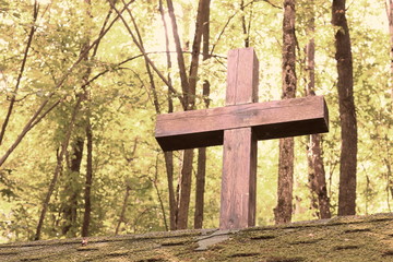 Wooden Christian religious cross on the background of green trees and rays of sunlight at dawn