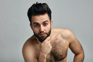 Handsome naked bearded guy with his hand on his chin standing in a sensual sexy pose, isolated on...