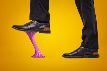 Violet bubble gum stuck to businessman shoes on yellow background