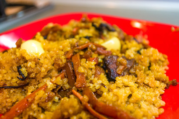 Uzbek pilaf with meat in a red plate on a wooden table, close up