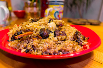 Uzbek pilaf with meat in a red plate on a wooden table, close up
