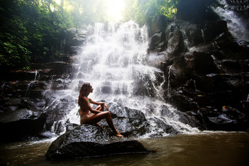 Woman practices yoga near waterfall in Bali, Indonesia