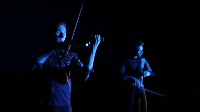 duet of young musicians playing the electric cello and electric violin on black background, isolated