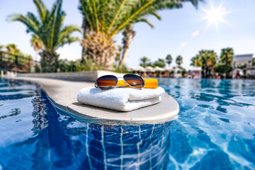 Obraz premium Summer sunglasses and white towel with swimming pool space 