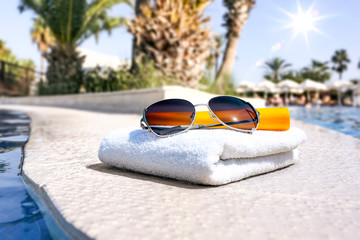 Summer sunglasses and white towel with swimming pool space 