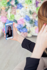 Young beautiful caucasian girl business woman in black suit touch hair and holding smartphone in blue case, make selfie photo. Back view, female beauty portrait famous blogger