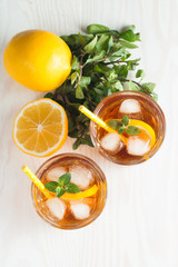 Refreshing citrus lemonade, summer drink. Ice tea with fresh lemon and mint on wooden background. Refreshment beverage concept.