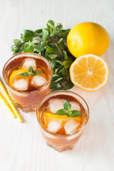 Refreshing citrus lemonade, summer drink. Ice tea with fresh lemon and mint on wooden background. Refreshment beverage concept.