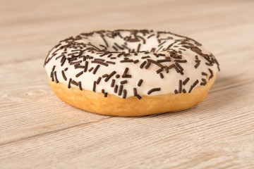 Fresh glazed donut with chocolate sprinkles on a wooden table.