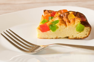 A piece of cottage cheese casserole with candied fruits on a white plate. Close up.