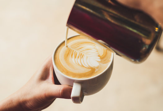 Closeup image of female barista holding and pouring milk for prepare cup of coffee, latte art, vintage color tone, coffee preparation and service concept, lifestyle