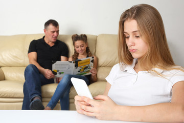 teenage girl looks in the phone alone on the background of family