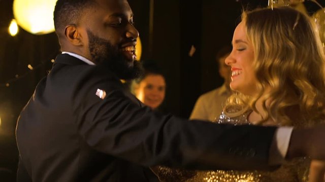 Happy multiracial man and woman dancing under falling confetti, celebration