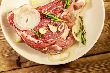 Marinated beef rib eye steak on bone with spices, onion and rosemary on wooden table