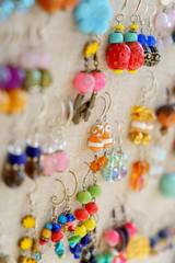 Many colorful earrings for sale at outside street market hanging on canvas, side view, vertical