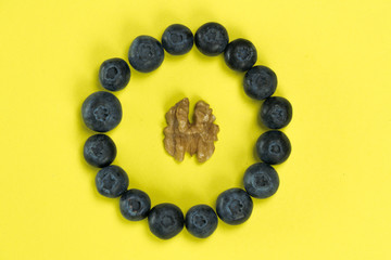 circle of organic blueberries with a walnut in the center on yellow background