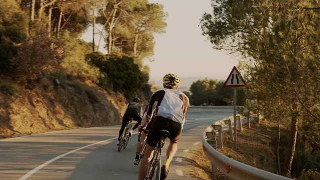 Two professional or amateur cyclists descend down mountain curvy road during golden hour sunset. Beautiful image of healthy sport lifestyle, romantic and dreamy view on excercise