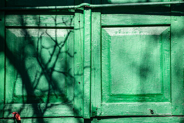 Old shutters with worn green red on a brick house on a Sunny day with a pattern of shadows from behind the tree. Simple Russian style