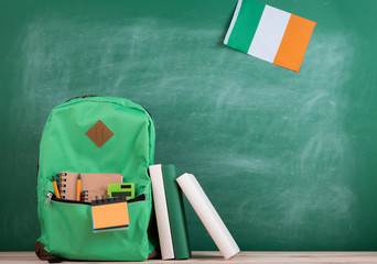 green backpack, flag of the Ireland, books and notebooks on the background of the blackboard