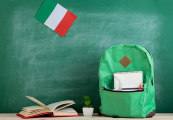 green backpack, flag of the Italy, books and notebooks on the background of the blackboard