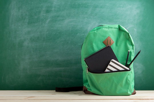 green backpack, black notebooks and pencils on the background of the blackboard