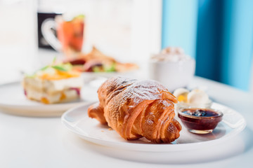 Beautiful fresh French croissants with jam on a white plate on a light background in the restaurant. Close-up. Space
