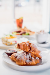 Beautiful fresh French croissants with jam on a white plate on a light background in the restaurant. Close-up. Space
