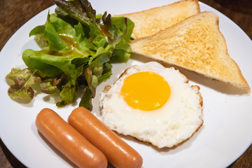 Delicious breakfast; fried egg, sausage, toast and salad on wooden table.