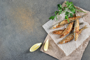 Fried smelt fish on paper. Slices of lemon and parsley next to the fish. View from above. Free...