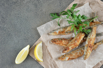 Fried smelt fish on paper. Slices of lemon and parsley next to the fish. View from above. Free...